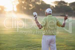 Rear view of mature golfer carrying golf club