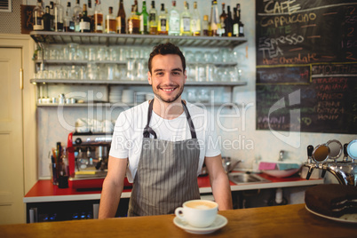 Portrait of confident waiter with coffee at counter in cafe