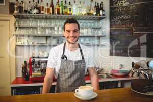 Portrait of confident waiter with coffee at counter in cafe