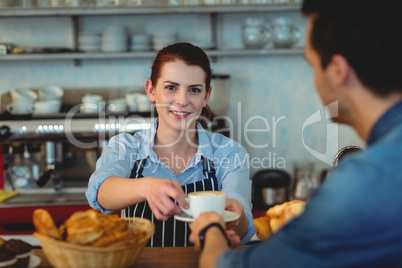 Portrait of confident barista giving coffee to customer at cafe