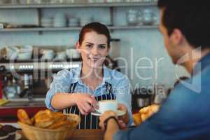 Portrait of confident barista giving coffee to customer at cafe