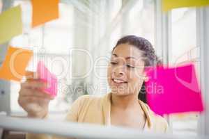Businesswoman sticking adhesive notes on glass window in creativ