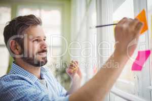 Smiling businessman writing on adhesive notes at office