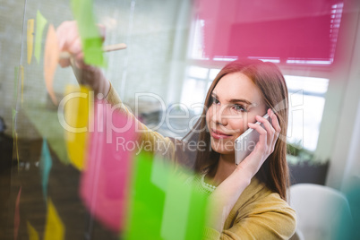 Smiling businesswoman talking on phone white writing on sticky n