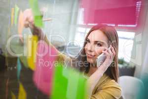 Smiling businesswoman talking on phone white writing on sticky n