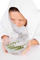 Woman steaming face with rosemary in bowl of water