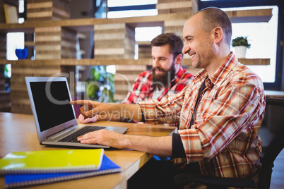 Creative male colleagues smiling while discussing over laptop