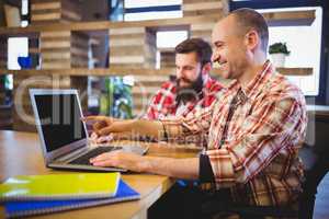 Creative male colleagues smiling while discussing over laptop
