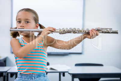 Portrait of elementary girl playing flute in classroom