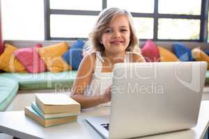Smiling girl using laptop in school library