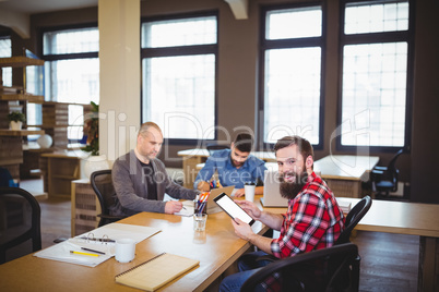 Businessman using tablet while colleagues working in office Businessman using tablet while colleagues working in office