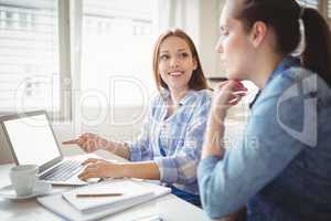 Young businesswoman discussing with colleague at desk in creativ
