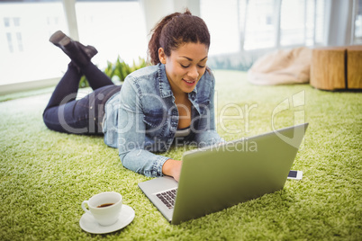 Businesswoman lying on carpet while using laptop in office