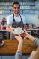 Happy waiter serving coffee to female customer at cafe