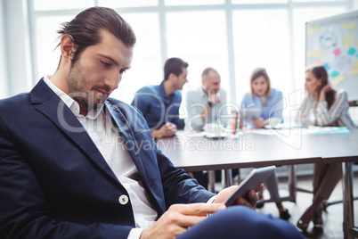 Confident businessman using digital tablet against colleagues