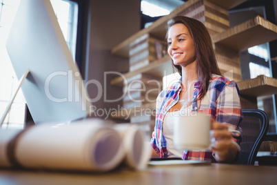Happy businesswoman holding cup while looking at computer