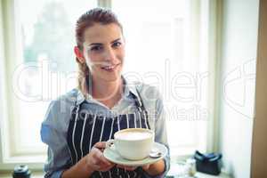 Portrait of happy waitress offering coffee at cafe