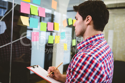 Businessman writing on document while looking at sticky notes