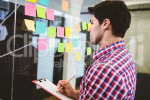 Businessman writing on document while looking at sticky notes