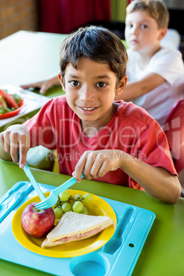 Smiling boy with classmates having meal