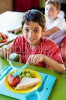 Smiling boy with classmates having meal