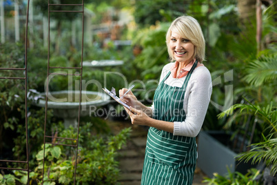 Portrait of female gardener writing in clipboard