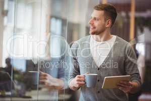 Businessman holding coffee cup with digital tablet in office