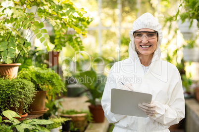 Female scientist smiling while writing on clipboard
