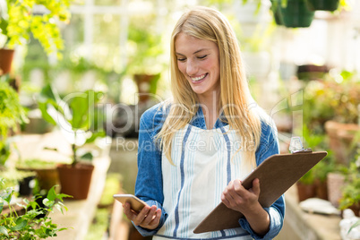 Female gardener using cellphone while holding clipboard
