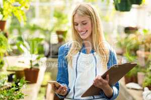 Female gardener using cellphone while holding clipboard