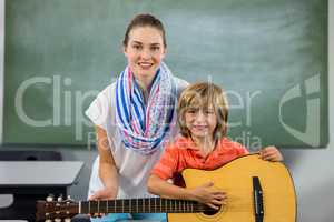 Portrait of young teacher assisting boy to play guitar