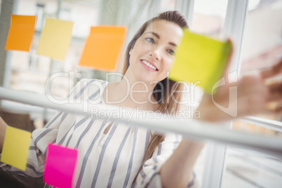 Happy businesswoman looking at adhesive notes in creative office