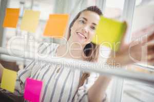 Happy businesswoman looking at adhesive notes in creative office