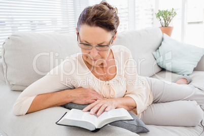 Mature woman reading book while resting on sofa