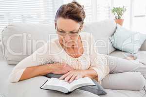 Mature woman reading book while resting on sofa