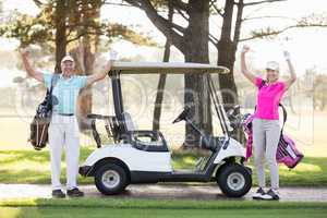 Portrait of smiling mature golfer couple with arms raised