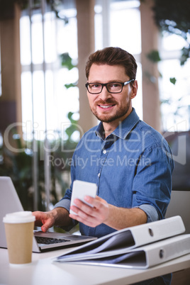 Portrait of confident businessman using cellphone at office