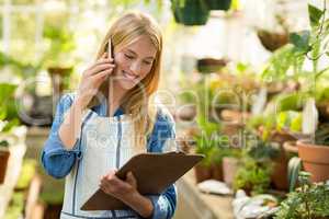 Female gardener talking on cellphone while looking at clipboard