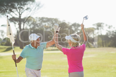 Cheerful mature golfer couple giving high five