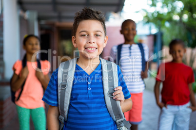 Happy schoolboy with classmates at school corridor