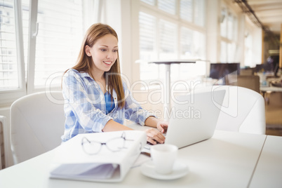 Businesswoman working on laptop at desk in creative office