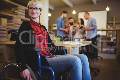 Confident woman on wheelchair while colleagues in background