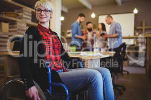 Confident woman on wheelchair while colleagues in background