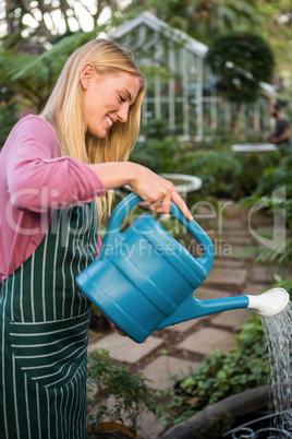 Side view of happy gardener watering plants against greenhouse