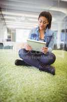 Businesswoman using digital tablet while sitting on carpet in cr