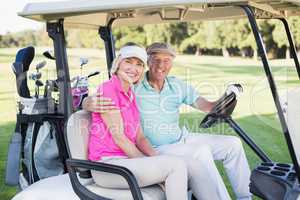 Cheerful mature couple sitting in golf buggy