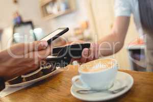 Close-up of customer with cellphone and barista with card reader