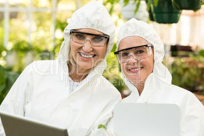 Smiling female coworkers wearing clean suit at greenhouse
