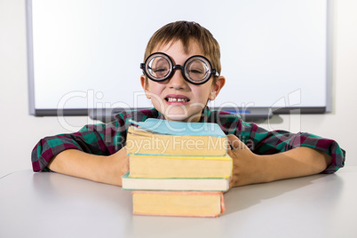 Happy boy holding books on table in classroom