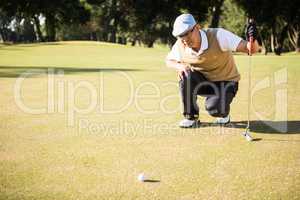 Side view of golfer crouching and looking his ball